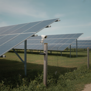 Solar panel field with a discreet security camera mounted on a post in a rural setting.
